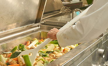 Koch in der Küche rührt einen großen Topf mit Suppengemüse